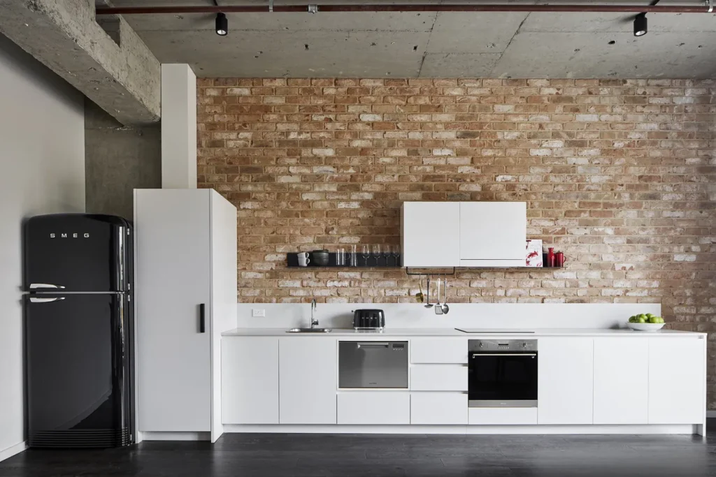Image shows a white kitchen with a repurposed brick wall.