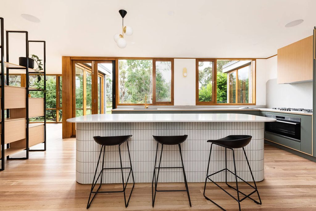 Image shows a modern, stylish kitchen with windows looking out over a garden.