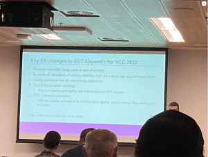 Photo of the Certifiers meeting, showing a powerpoint slide with the heading "Key Energy Efficiency Changes to ACT Appendix for NCC 2022". The slide has dot points summarising specific ACT energy efficiency legislation changes.