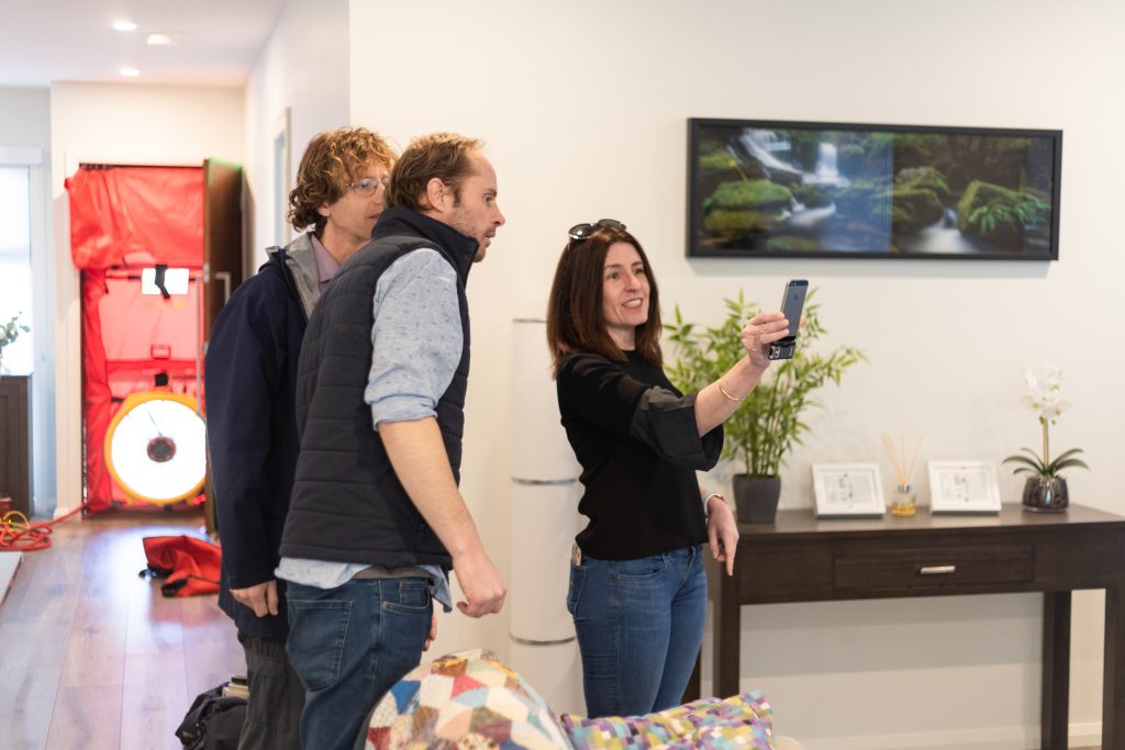 Image of the Powerhaus team assessing a cold house, looking at a phone. With a blower door set up in the background.