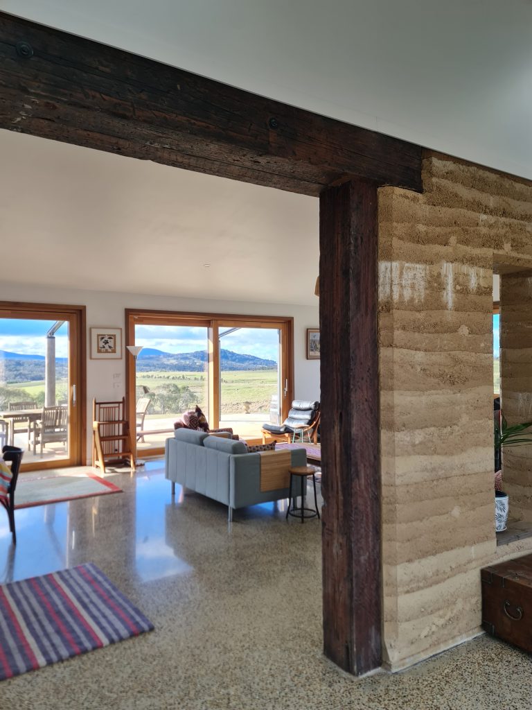 View through the sustainable off-grid farmhouse from the inside, showing a rammed earth wall through to the north-facing living-room.