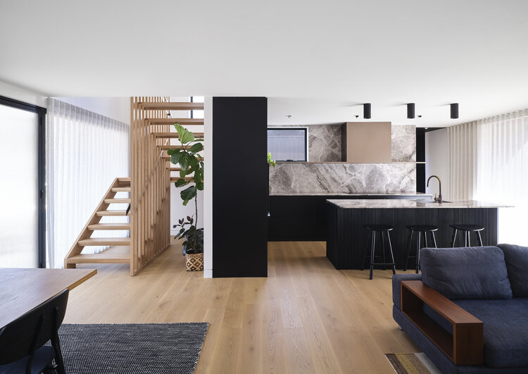 View of light-filled lounge room, kitchen and stairwell in Ziwa House.
