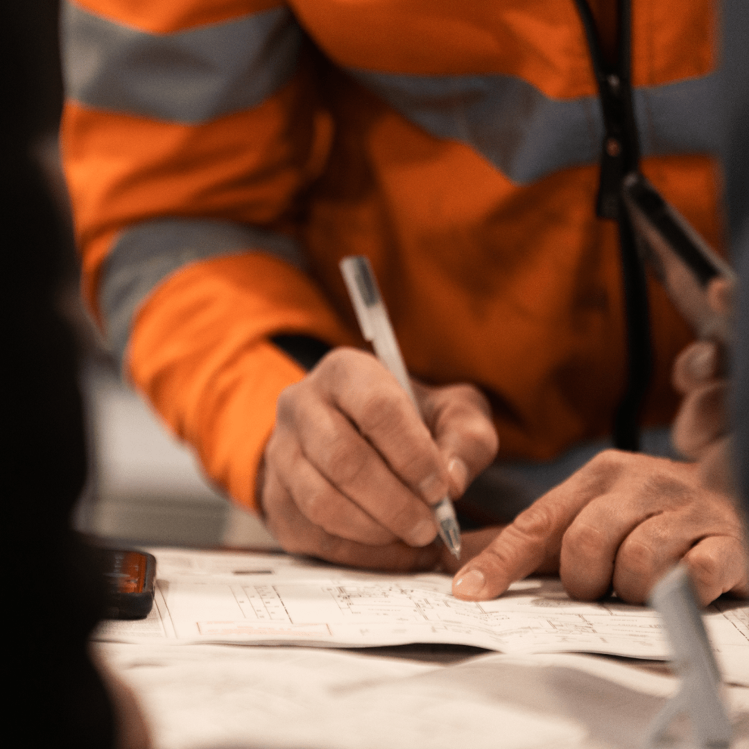 Powerhaus Image of a person in high-vis workwear drawing on house plans.