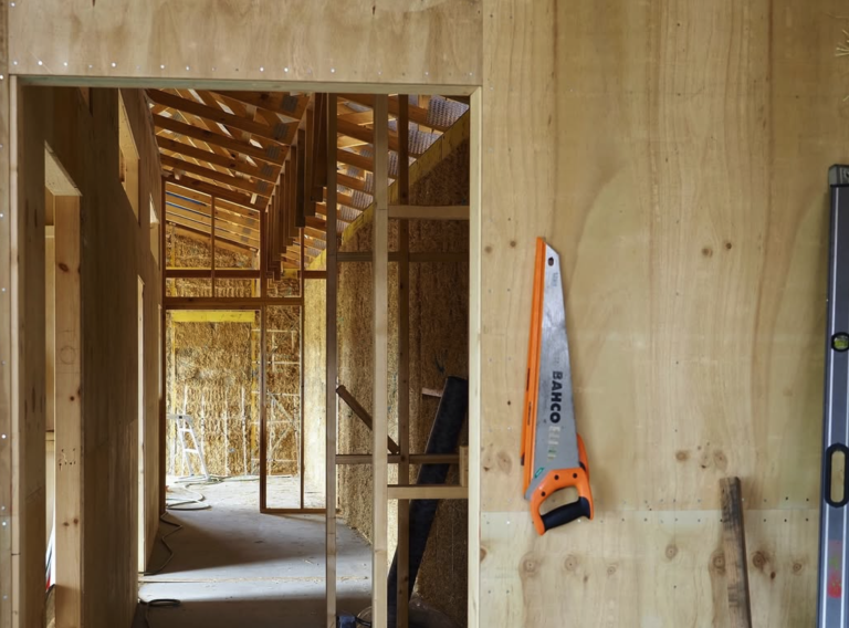 Image shows the inside of a strawbale house under construction with plywood wall cladding.