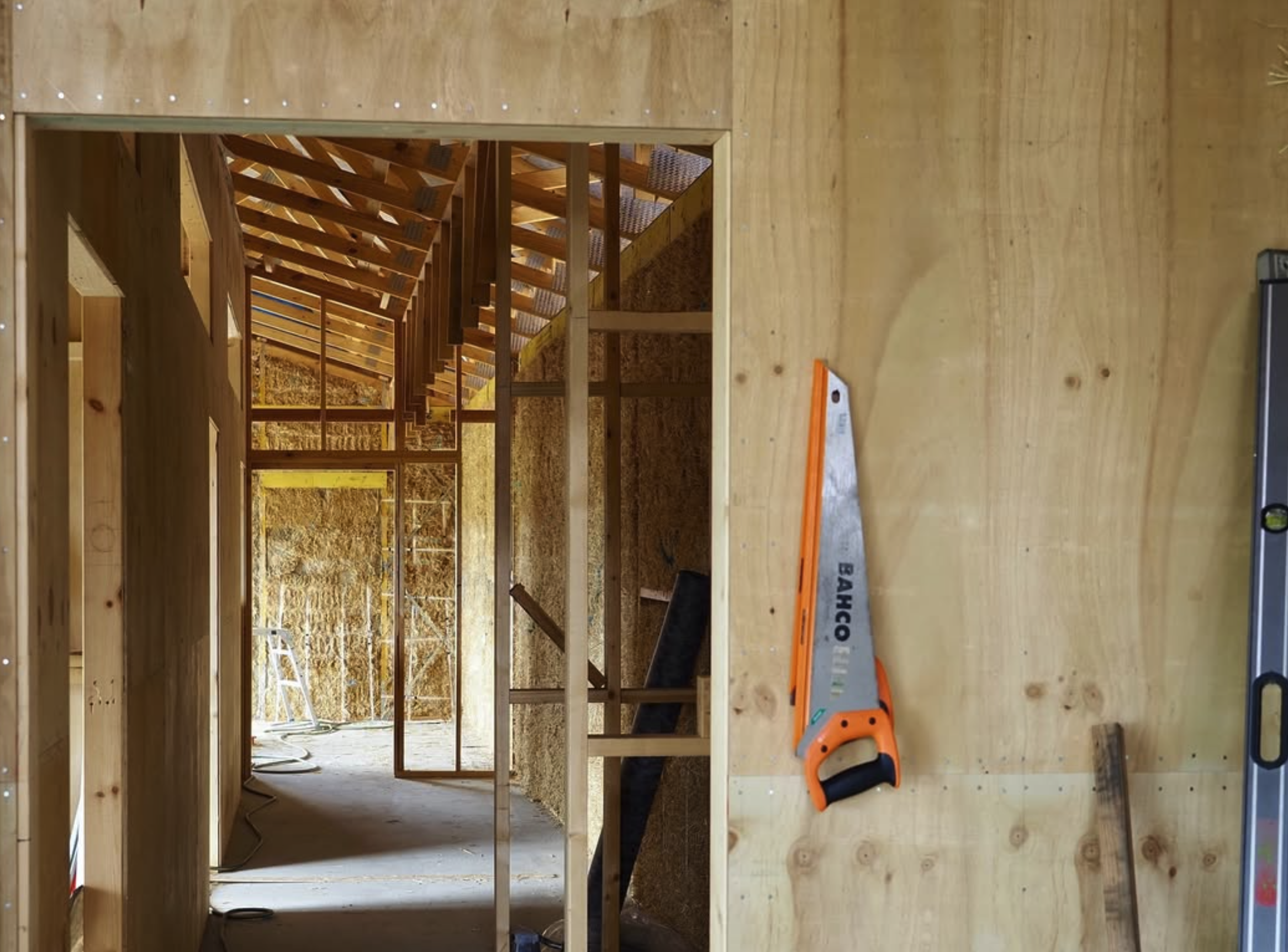 Image shows the inside of a strawbale house under construction with plywood wall cladding.